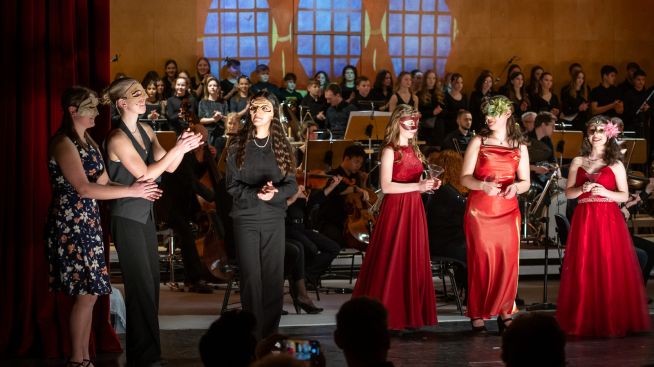 Im Vordergrund sind die Darstellerinnen von Juliette, Amelie, Antonia sowie Gäste des Maskenballs zu sehen. Im Hintergrund sieht man die Musiker und Chöre.