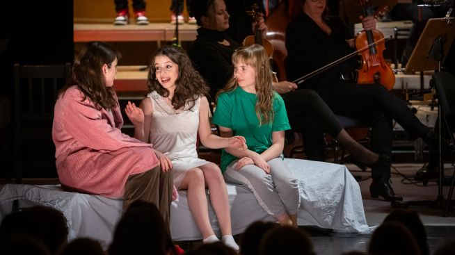 Auf dem Foto sind die Darstellerinnen der Juliette. Amelie und Antonia in ihren Schlafanzügen zu sehen. Im Hintergrund sieht man die Musiker des Loh-Orchesters.